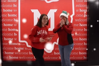 At Miami University, as admissions staff person dressed as an elf hands admissions envelopes to a student wearing a red Miami sweatshirt.