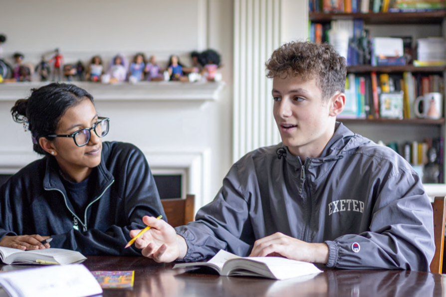 Two Exeter students sit at a table, books open in front of them in discussion.