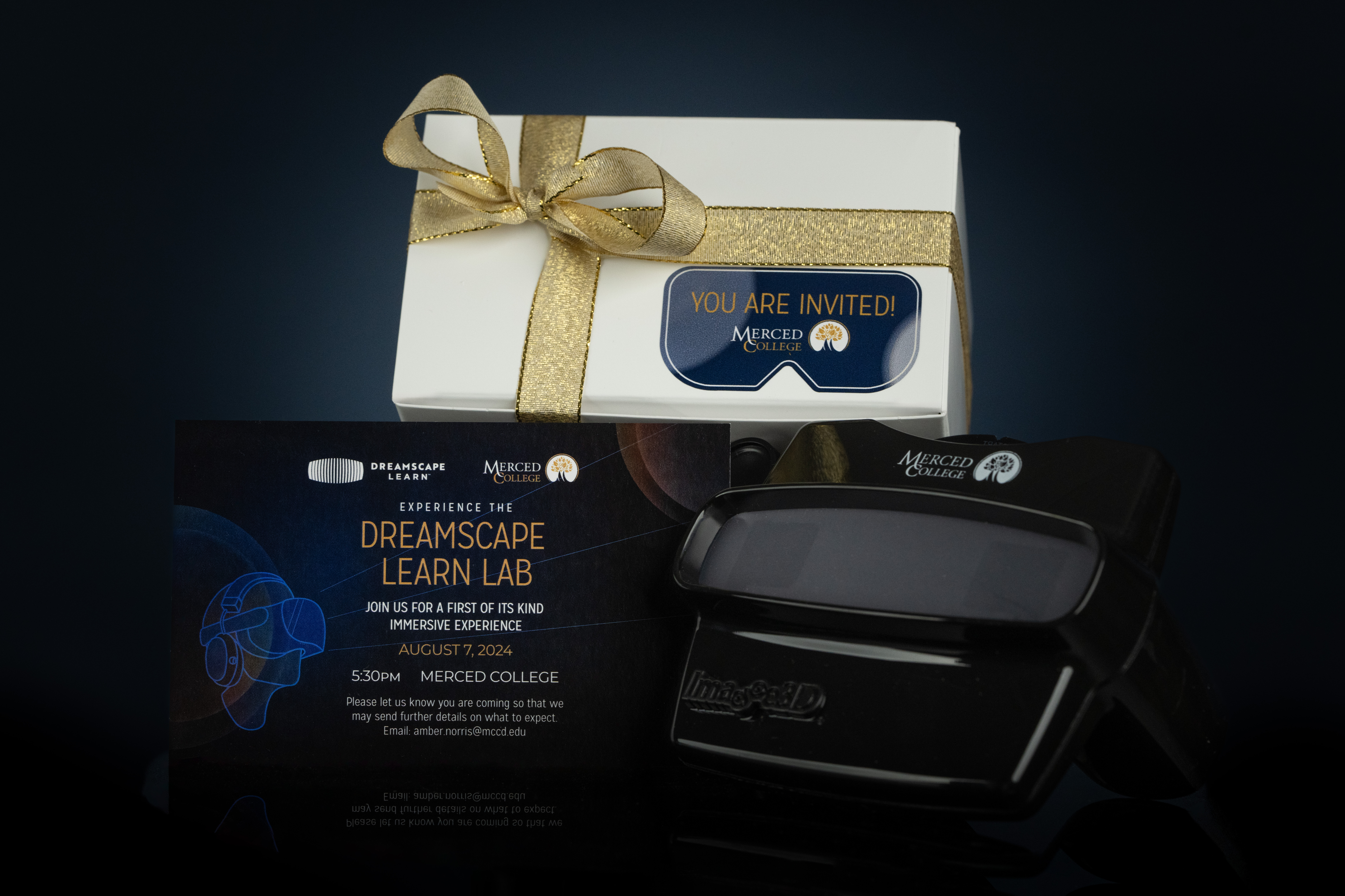 A photo of the white box tied with gold ribbon that Merced's invitation to Dreamscape Live (also pictured) and a black, branded ViewMaster (also pictured) were delivered in.