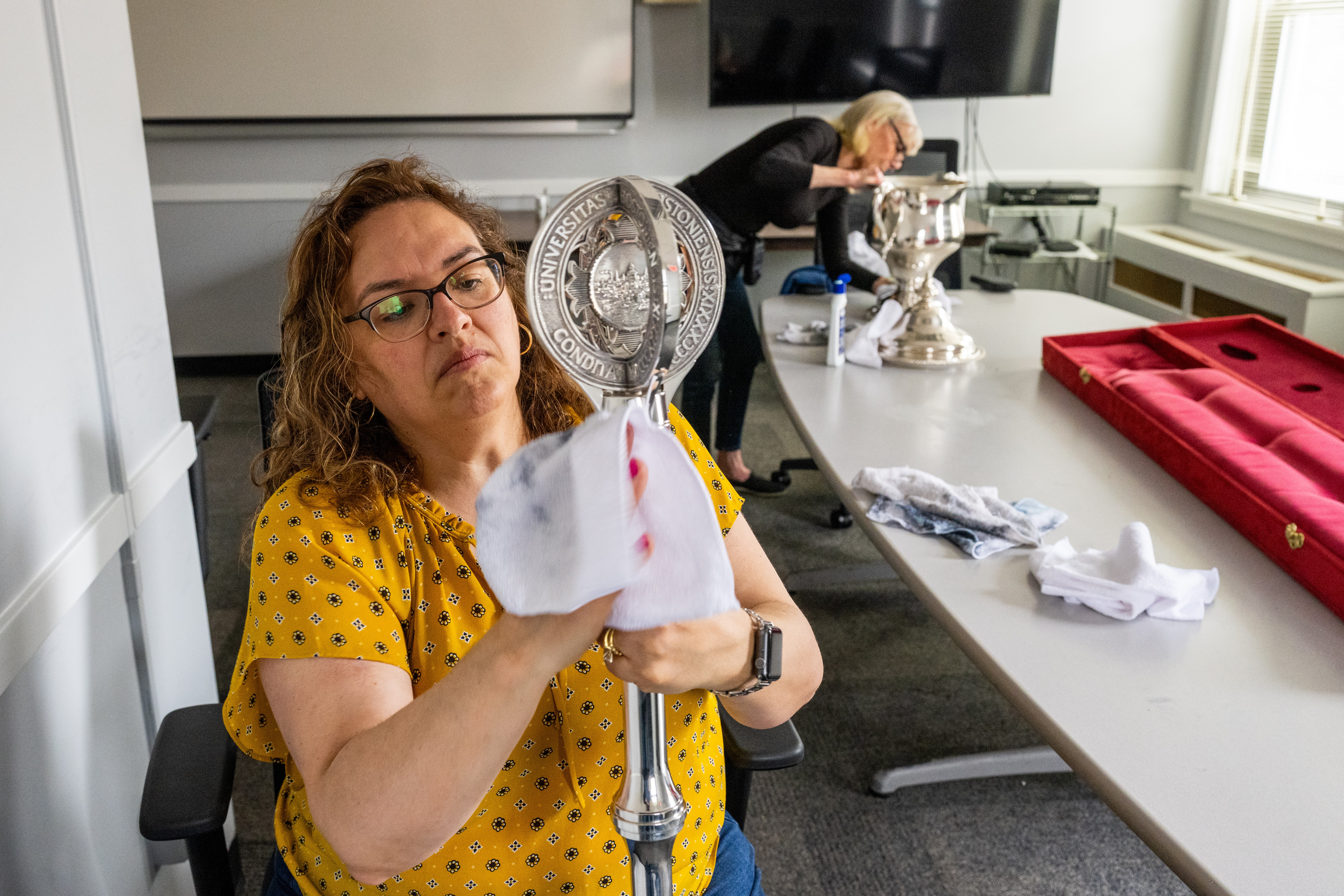 A woman cleans a metal staff that is used for Boston University's commencement.
