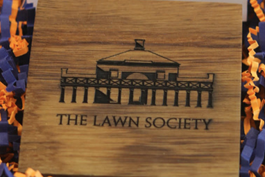 A block of wood engraved with the image of a UVA campus building and the words, "The Lawn Society."