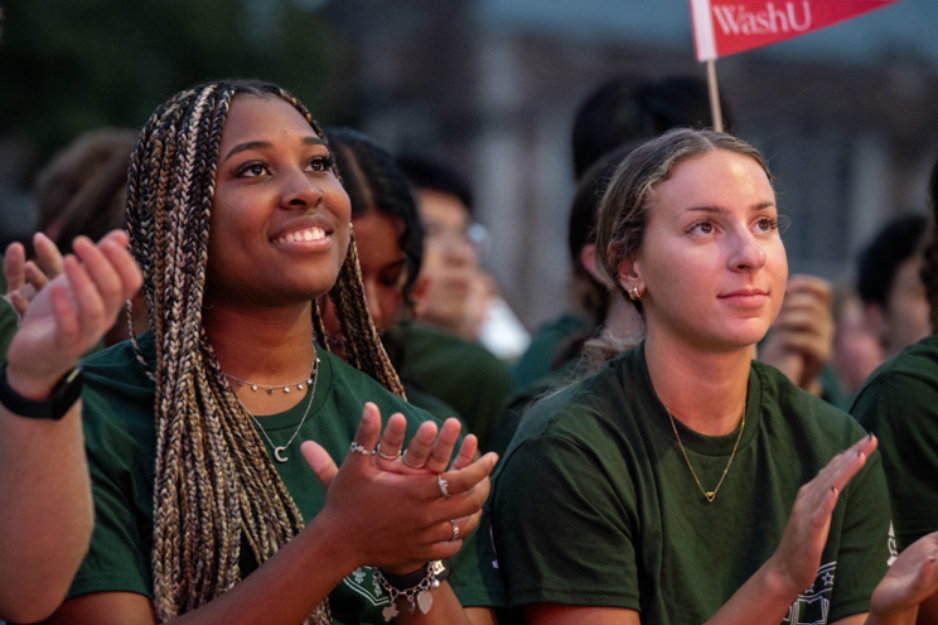 Two Washington University in St. Louis students wearing matching green T-shirts clap at an event.