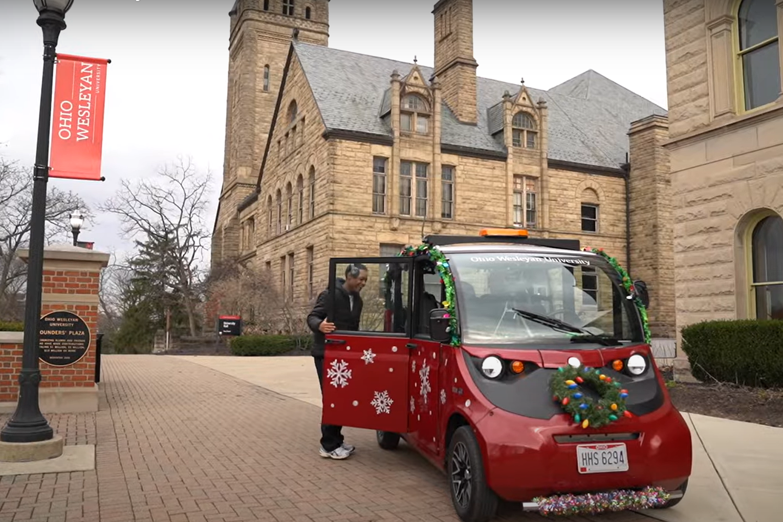 On the Ohio Wesleyan University campus, a red campus cab car, decorated for the holidays with tinsel, lights, and a wreath, picks up a student.