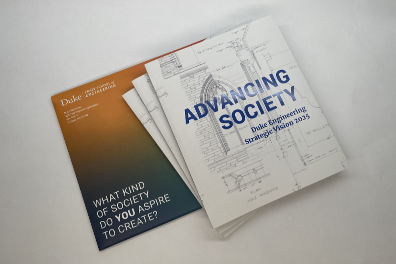 A photo of the Duke Engineering Strategic Vision publication and the orange and blue ombre colored envelope it was sent in. The cover of the publication features blue-colored text that reads, "Advancing Society," and a white background with black architectural drawings.