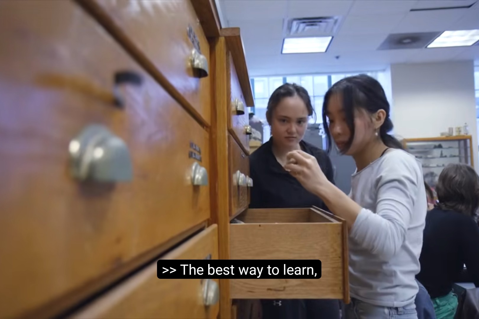 Two students look inside a drawer in a science classroom. One lifts out a rock.
