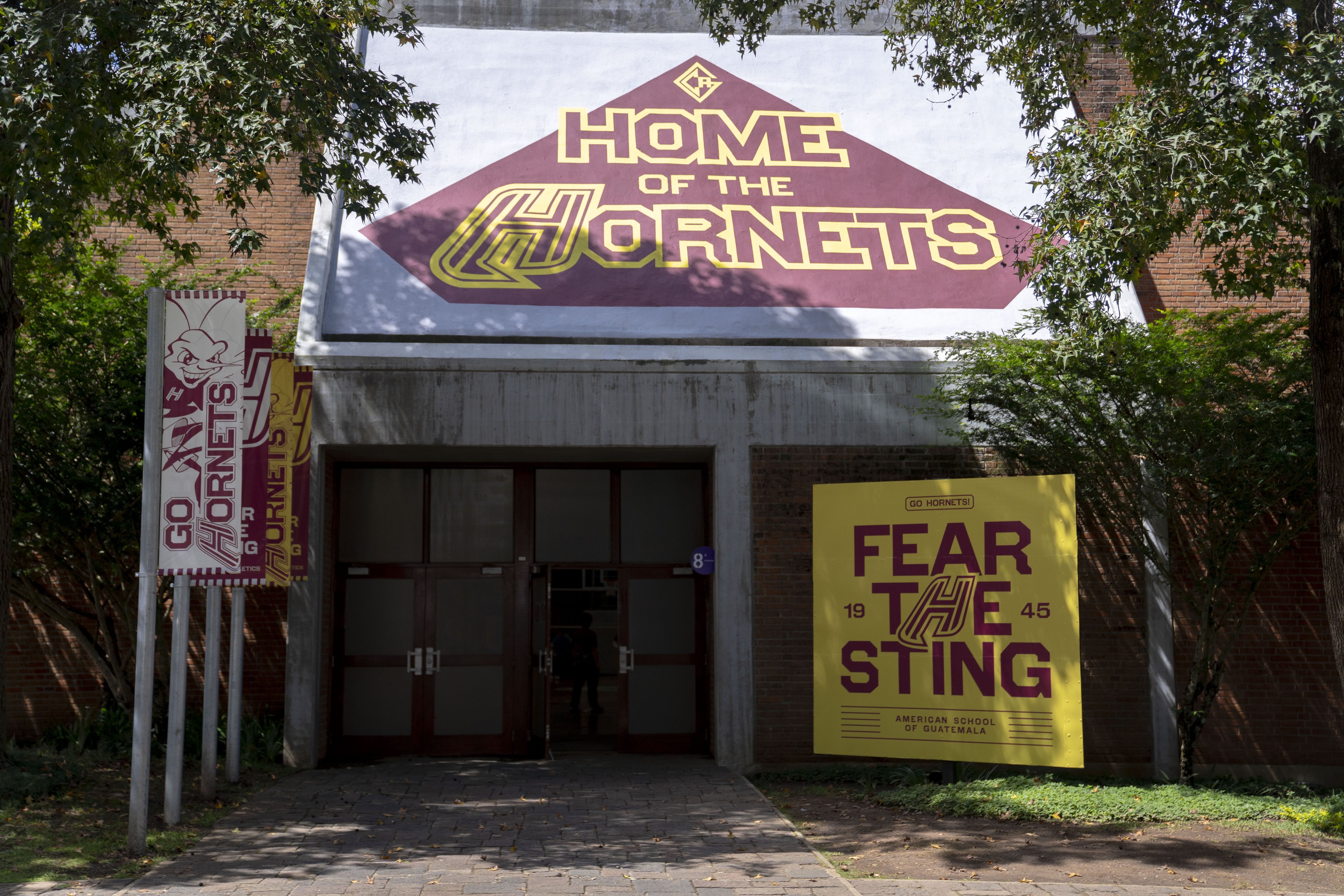 A photo of an entrance to a building. Above the doors is a red and yellow "Home of the Hornets" graphic. To the right of the door, a sign that reads, "Fear the Sting," and to the left a series of banners that read, "Go Hornets."