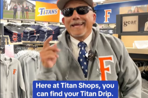 Fullerton's president stands in the university's gift shop wearing university merch. The caption reads, "Here at Titan Shops, you can find your Titan Drip."