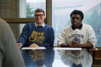 Two Kent State students wearing Kent State sweatshirts sit across the table from a campus leader as they pitch their video script.