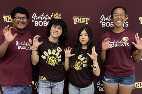 Four TXST students pose for a photo, holding their hands up in claw-like pose.