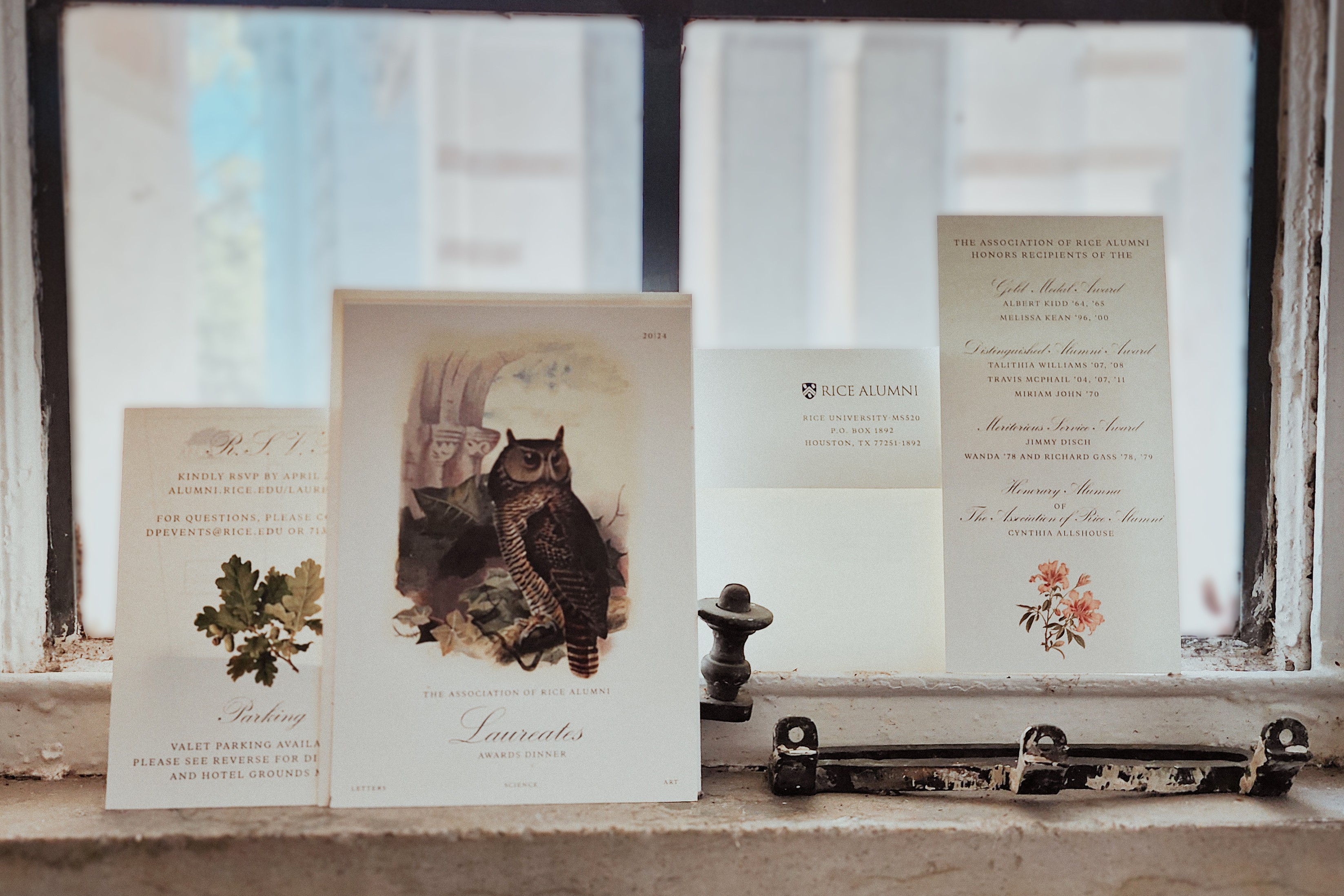 A photo shows an invitation and its various parts propped up against a window pane. The front of the invitation shows an illustration of an owl.