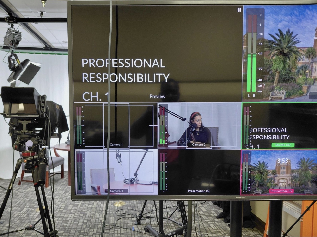 A photo shows a screen that displays multiple camera set-ups for the recording of a video. Behind the screen is a camera and chairs in front of a white back drop.
