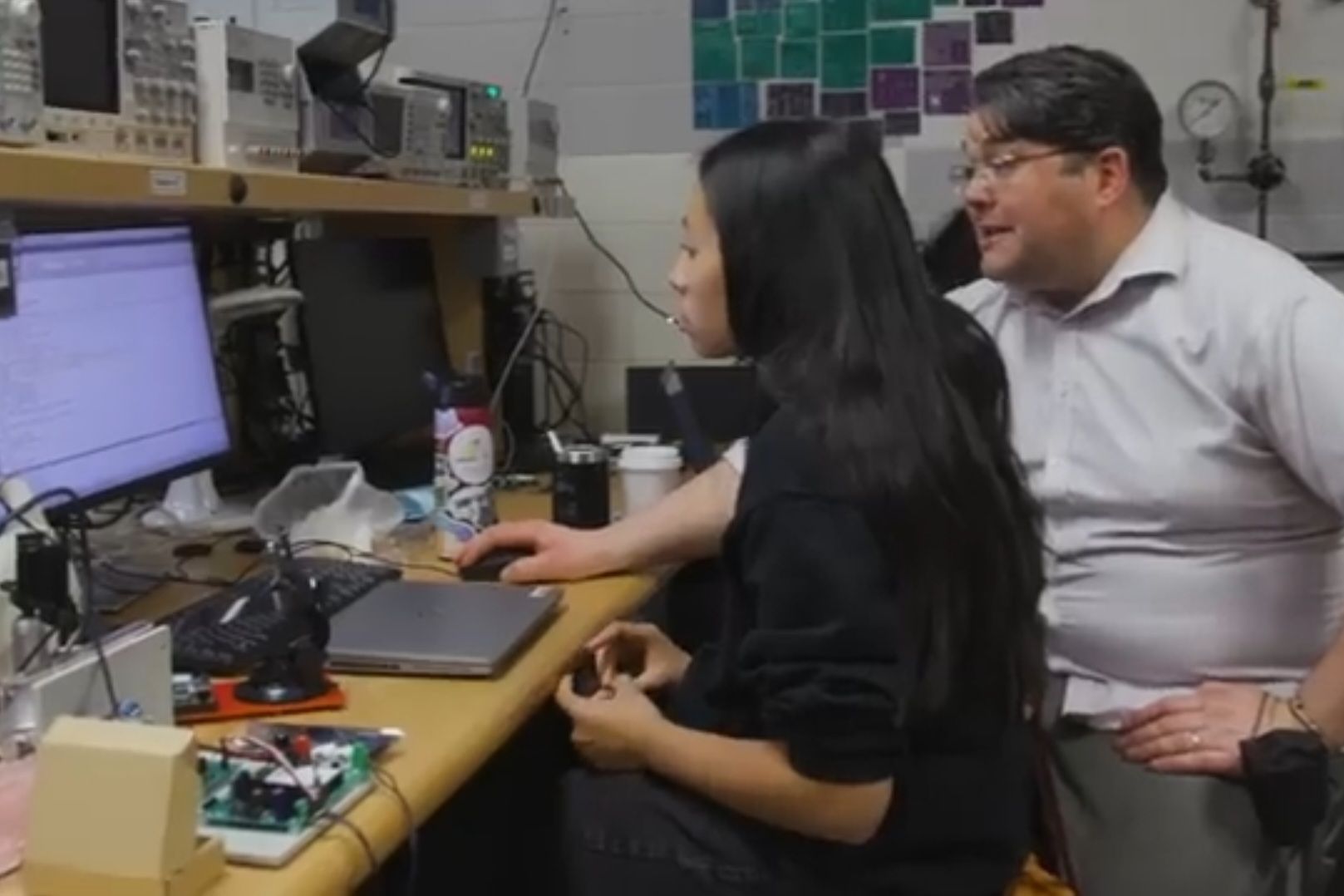 A student and instructor sit at a computer in a mechanical engineering lab.