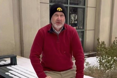 Tippie College of Business Associate Dean of Undergraduate Students, Charles Wayne Keene sits on a snow-covered bench outside an academic building. He wears a University of Iowa beanie and a red pullover.