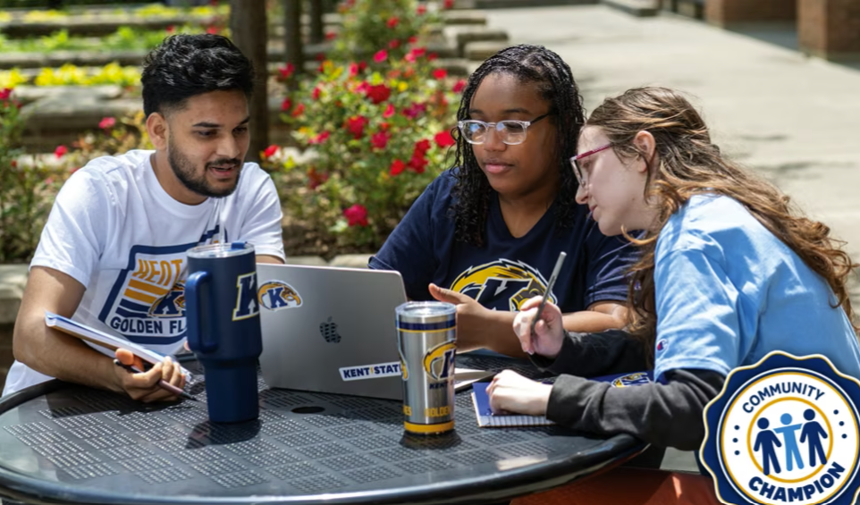 A photo of three Kent State students sitting around a table outside on campus doing homework.