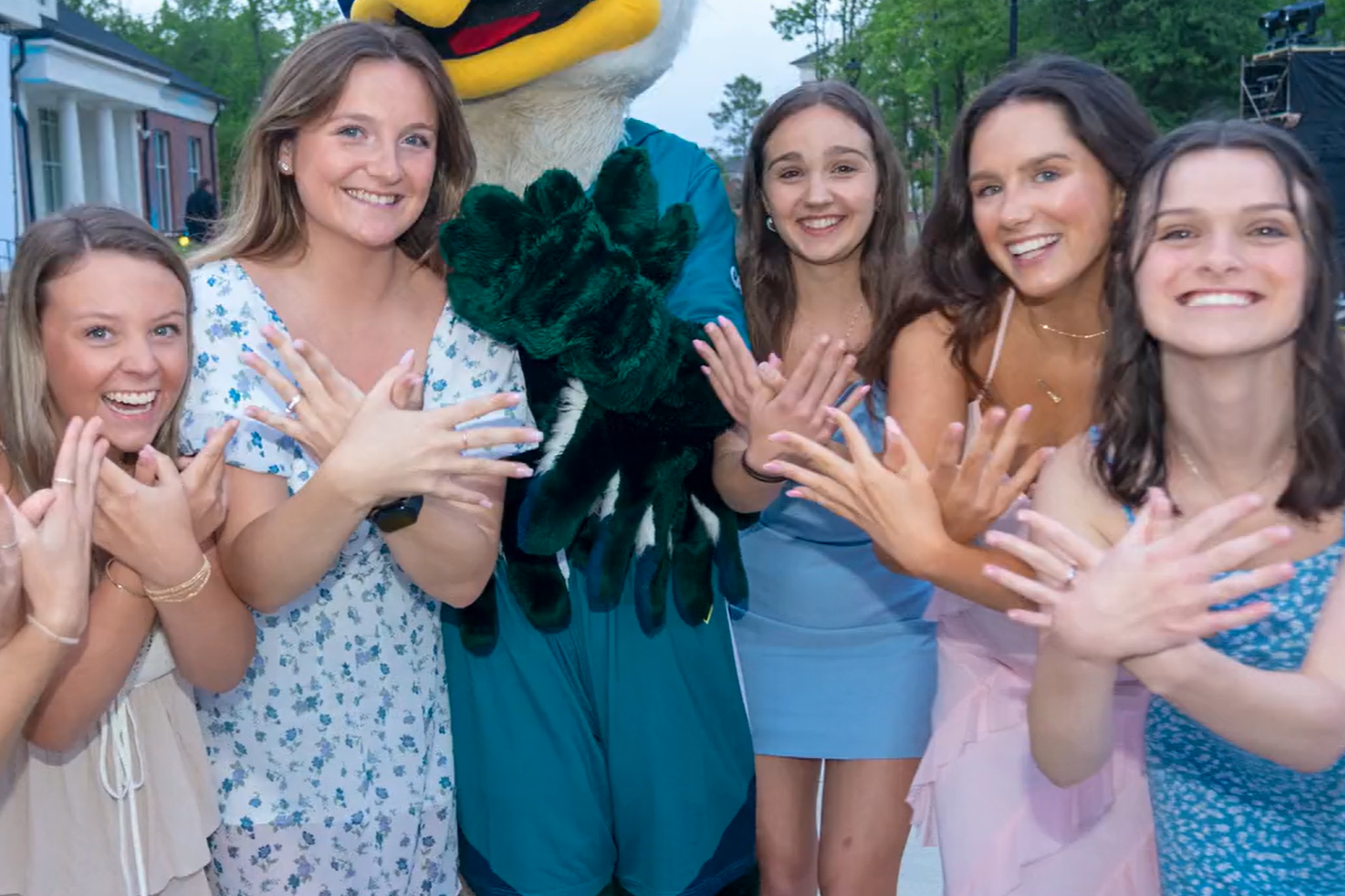 Five women all wearing summer dresses pose with UNCW's mascot (a seahawk), their hands forming wings.