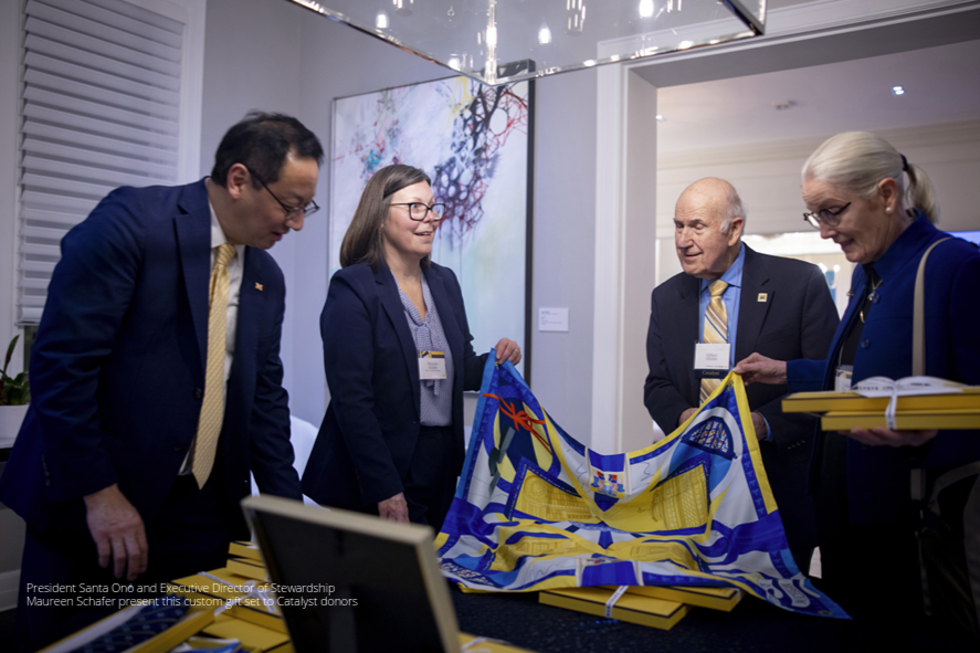 Two U-M advancement staff present the Catalyst scarf to two donors.