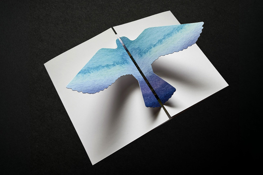 A white invitation with a blue-ombre-colored bird pop-out.