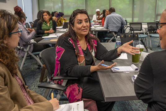 Diverse faculty discuss in small groups in a classroom.