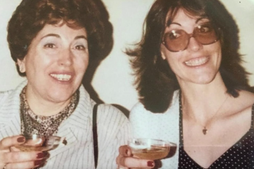 A mother and daughter smile for the camera. Each holds a coupe glass filled with a pink colored drink.