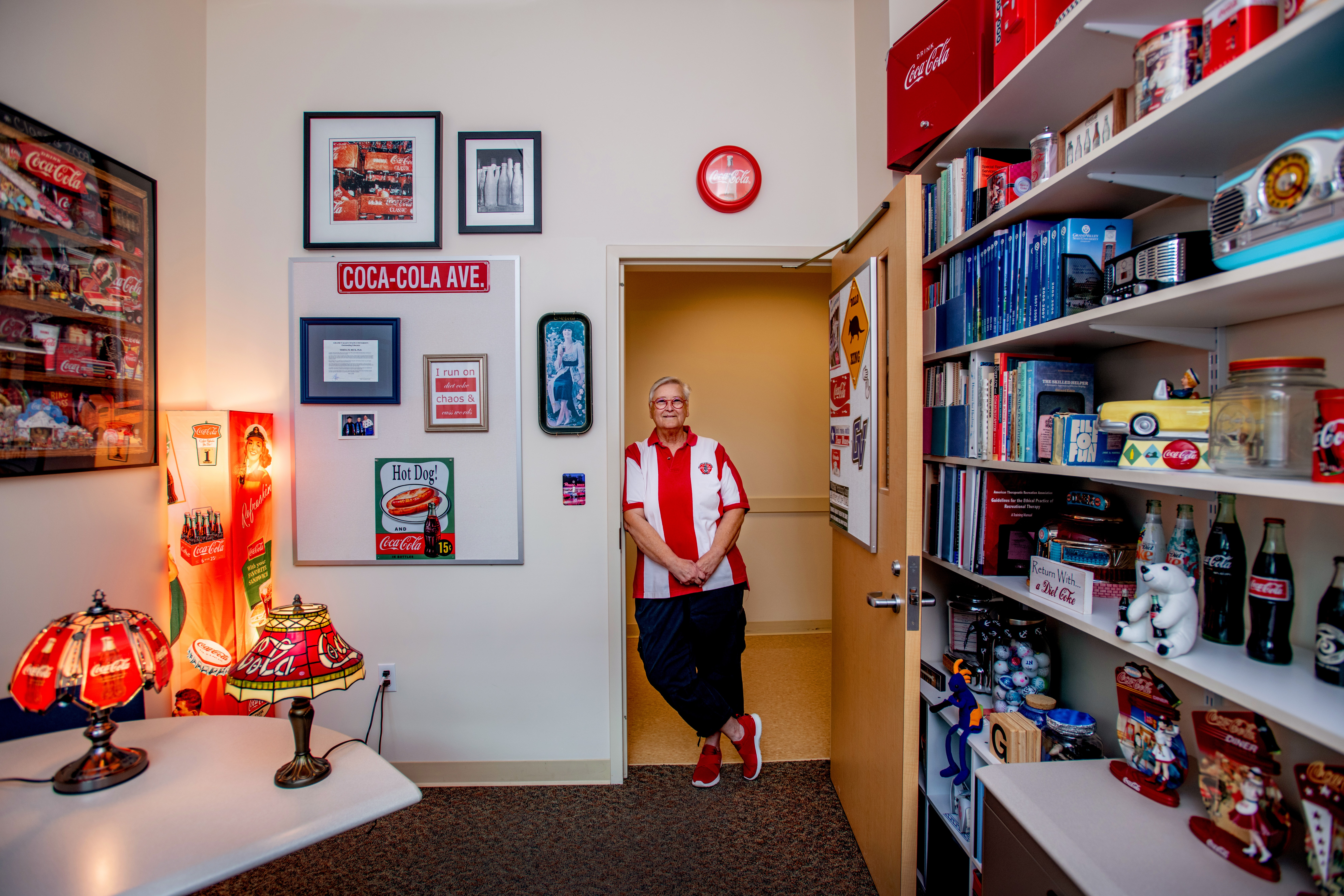 A person standing in the doorway of their office filled with Coca-Cola memorabilia.