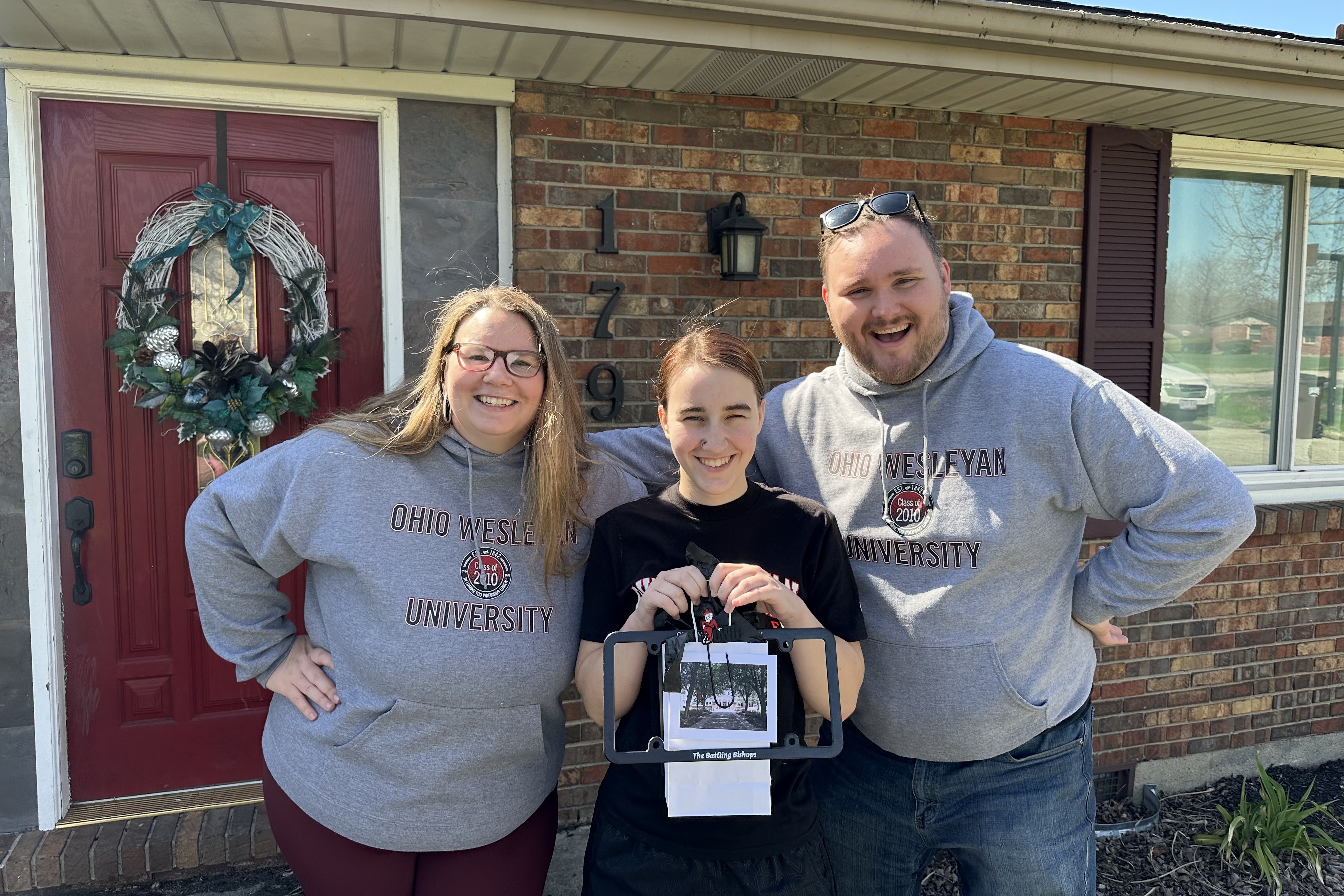 Two people wearing matching gray Ohio Wesleyan University Class of 2010 sweatshirts pose with a prospective student holding a goody bag.