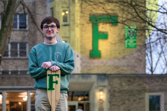 A photo of Ryan Murphy '26 standing in front of Notre Dame's Fisher Hall holding an oar with a green "F" on it.