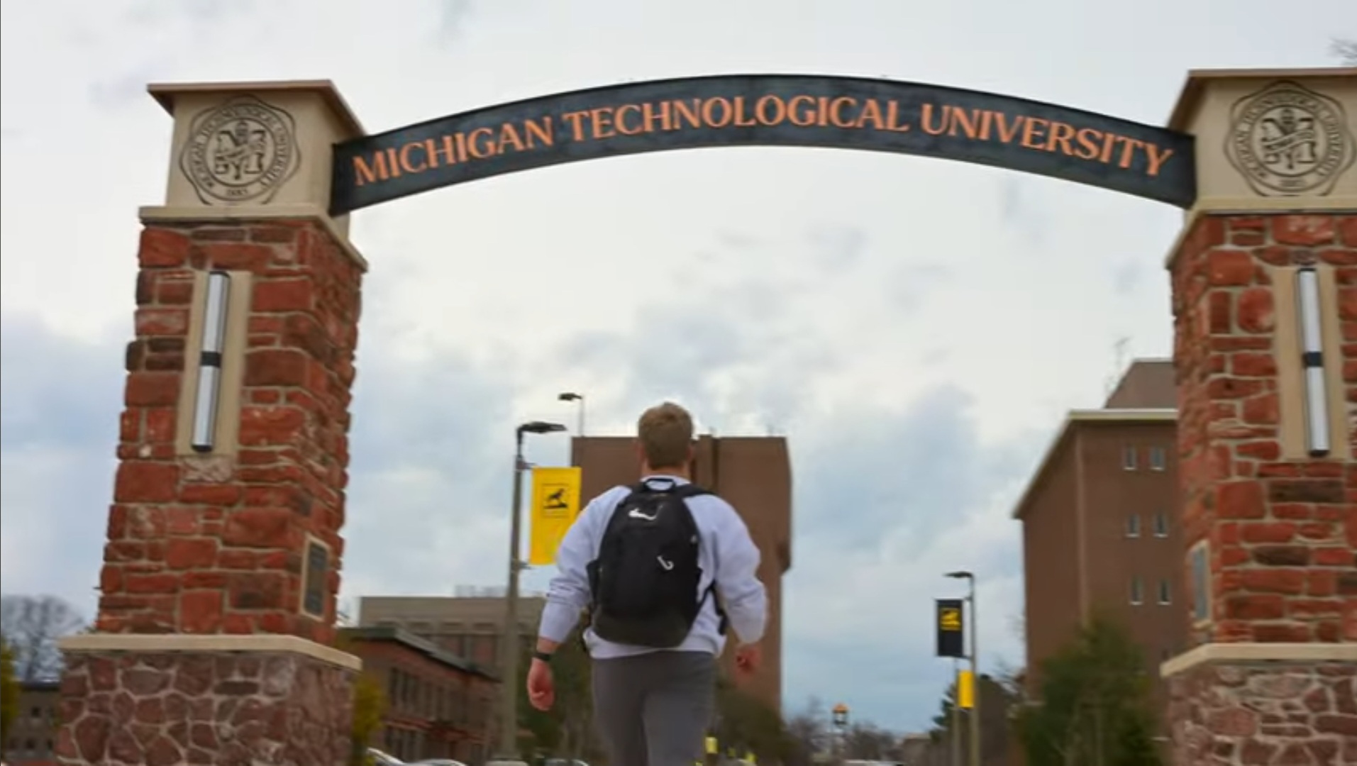 A screenshot from Michigan Tech's Passion Meets Purpose video shows a male student walking beneath an archway that reads, "Michigan Technological University."