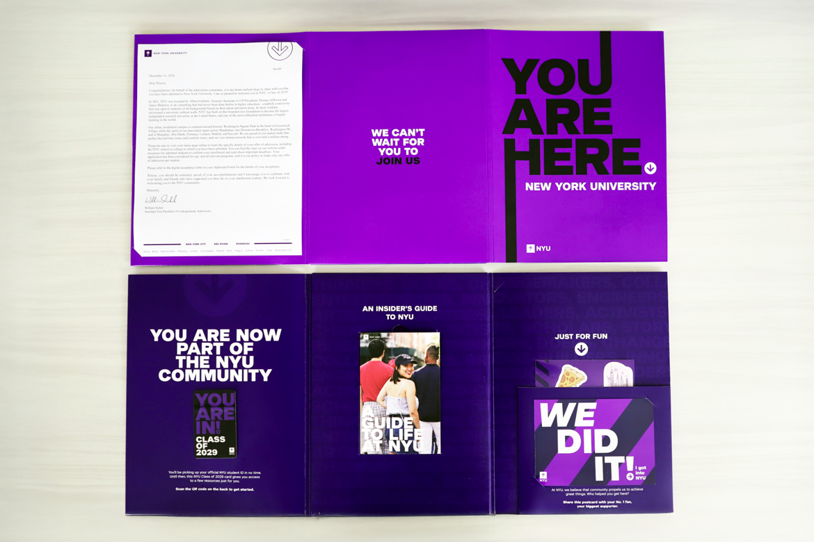 A photo of NYU's admitted student brochure. The cover reads "You Are Here." Inside are pockets with materials including an acceptance letter, guidebook, and stickers.