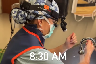 A medical resident scrubs in for surgery. She wears a light blue scrub cap with turtles on it.