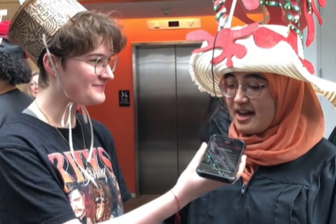 Two Smith College students wearing homemade hats. One holds a phone out to the other as a microphone.