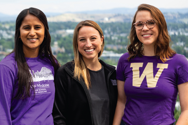 Three University of Washington students pose for camera wearing purple and black UW gear. 