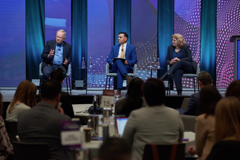 At Tech Horizons, three people sit in chairs on stage in front of a crowd seated at circular tables.