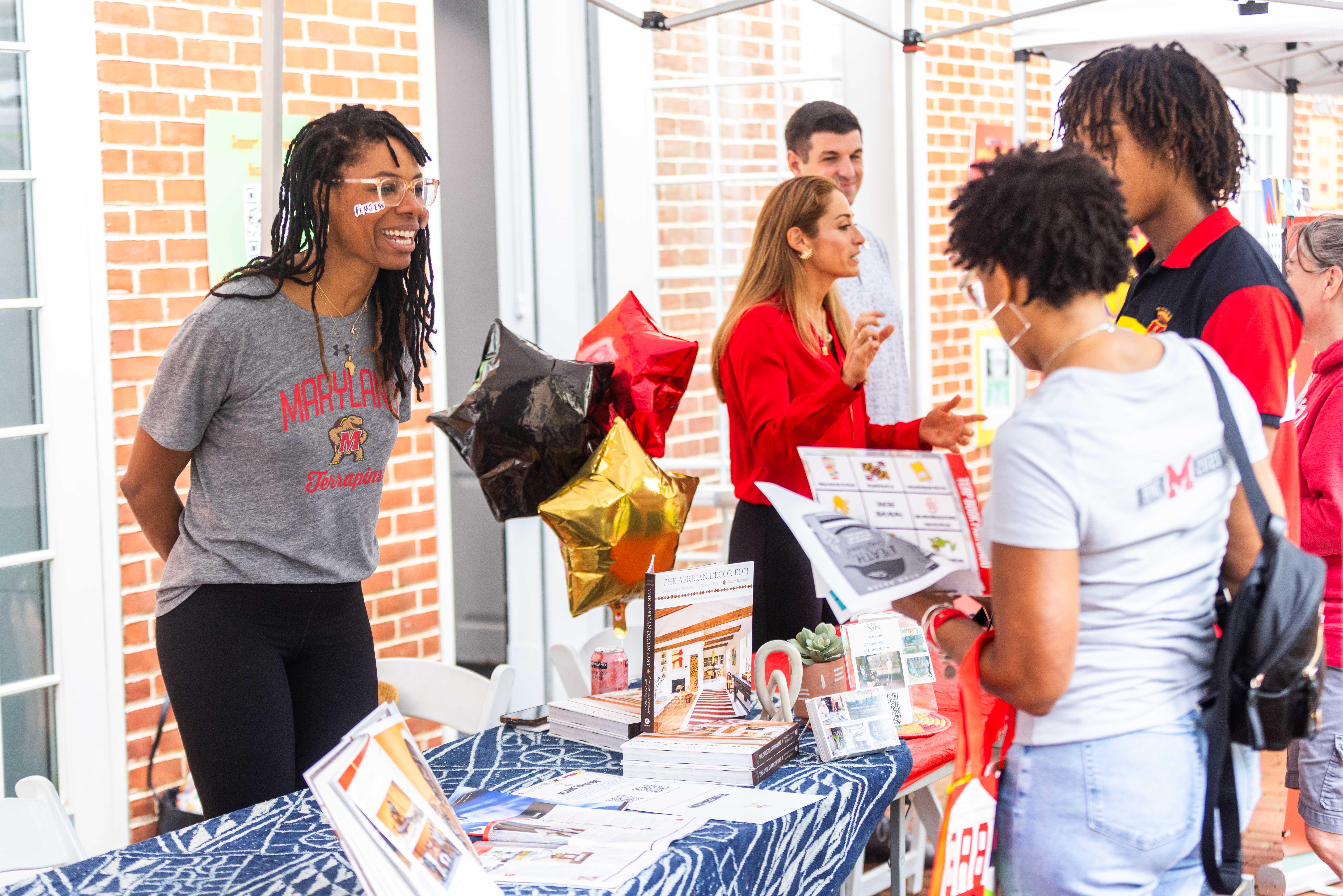 A photo from the Terp Author Book Fair. Two people look at flyers on one side of a table.