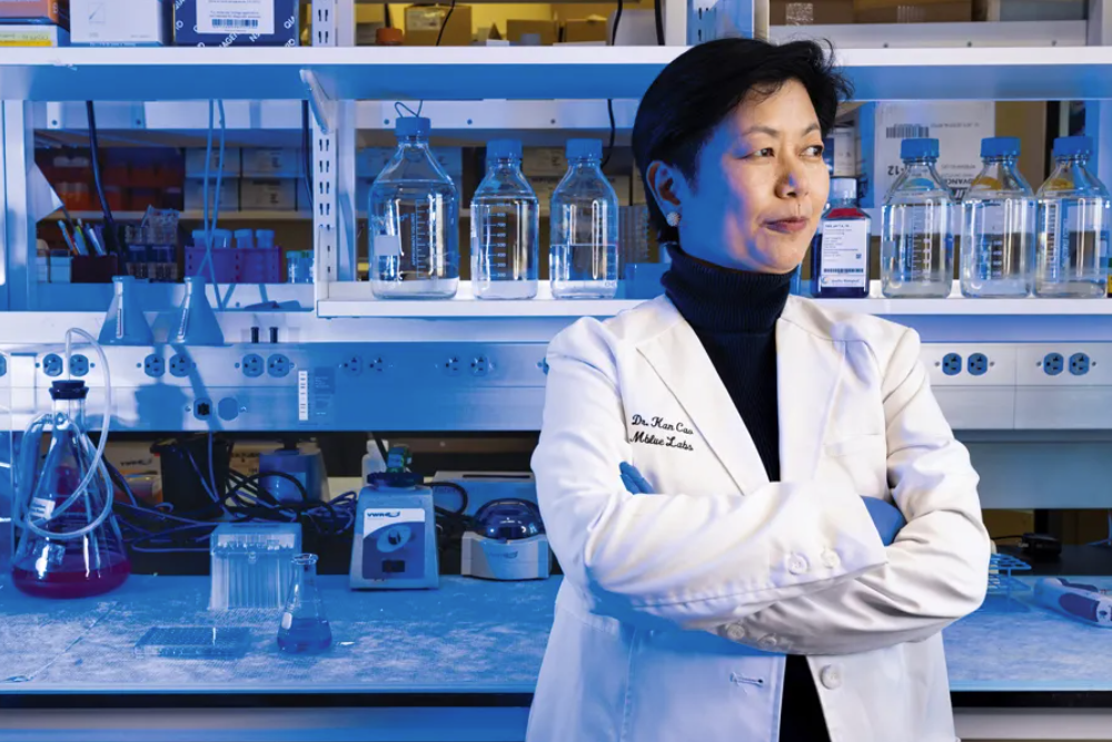 Kan Cao, a professor with UMD’s Department of Cell Biology and Molecular Genetics, poses for a photo in a lab wearing a white lab coat with her arms crossed.