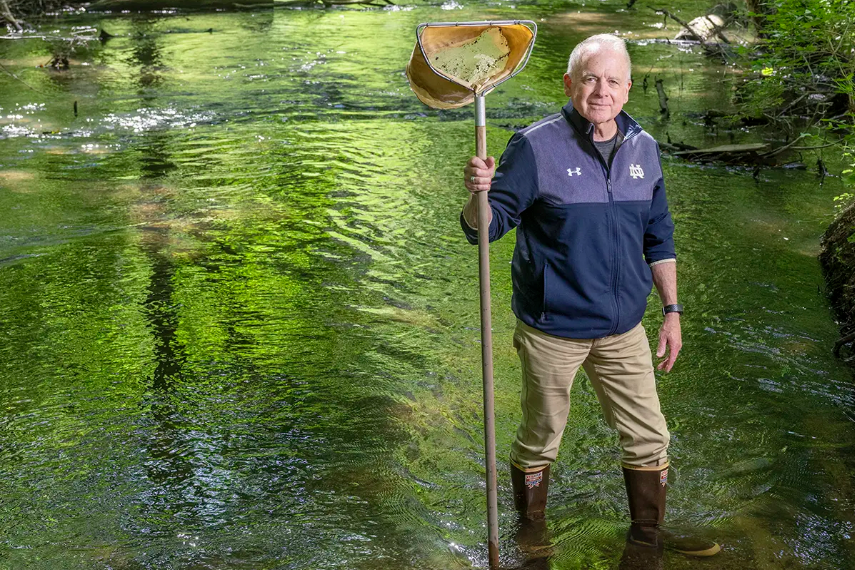 Notre Dame Professor Gary Lamberti stands in a shallow river holding a net.