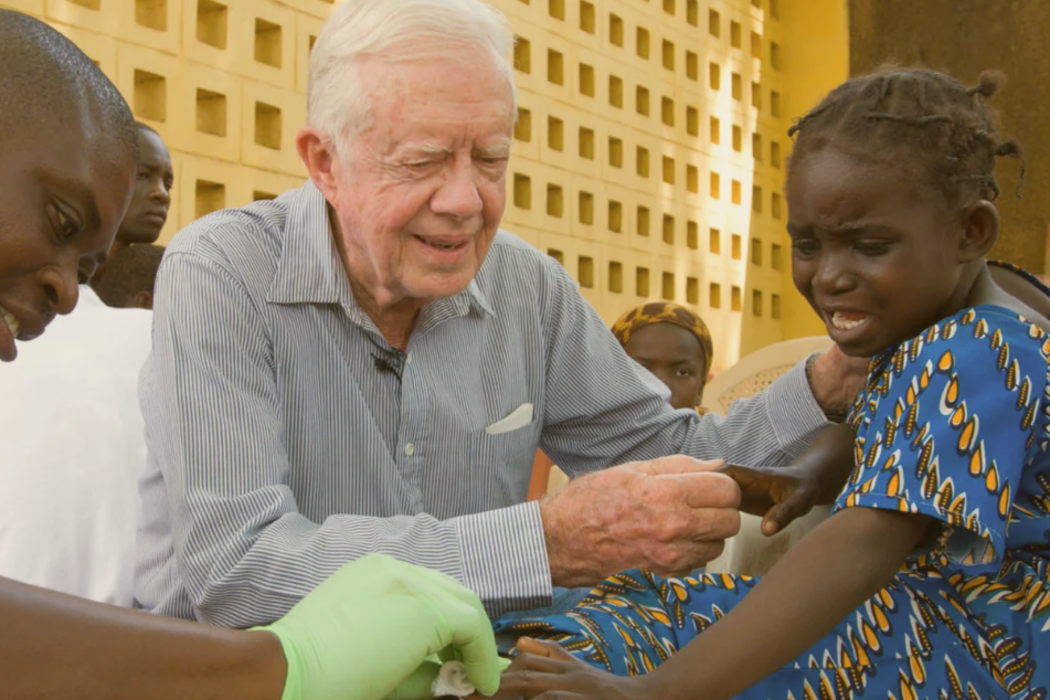 President Jimmy Carter holds the hand of a Black girl being treated for Guinea worm disease.