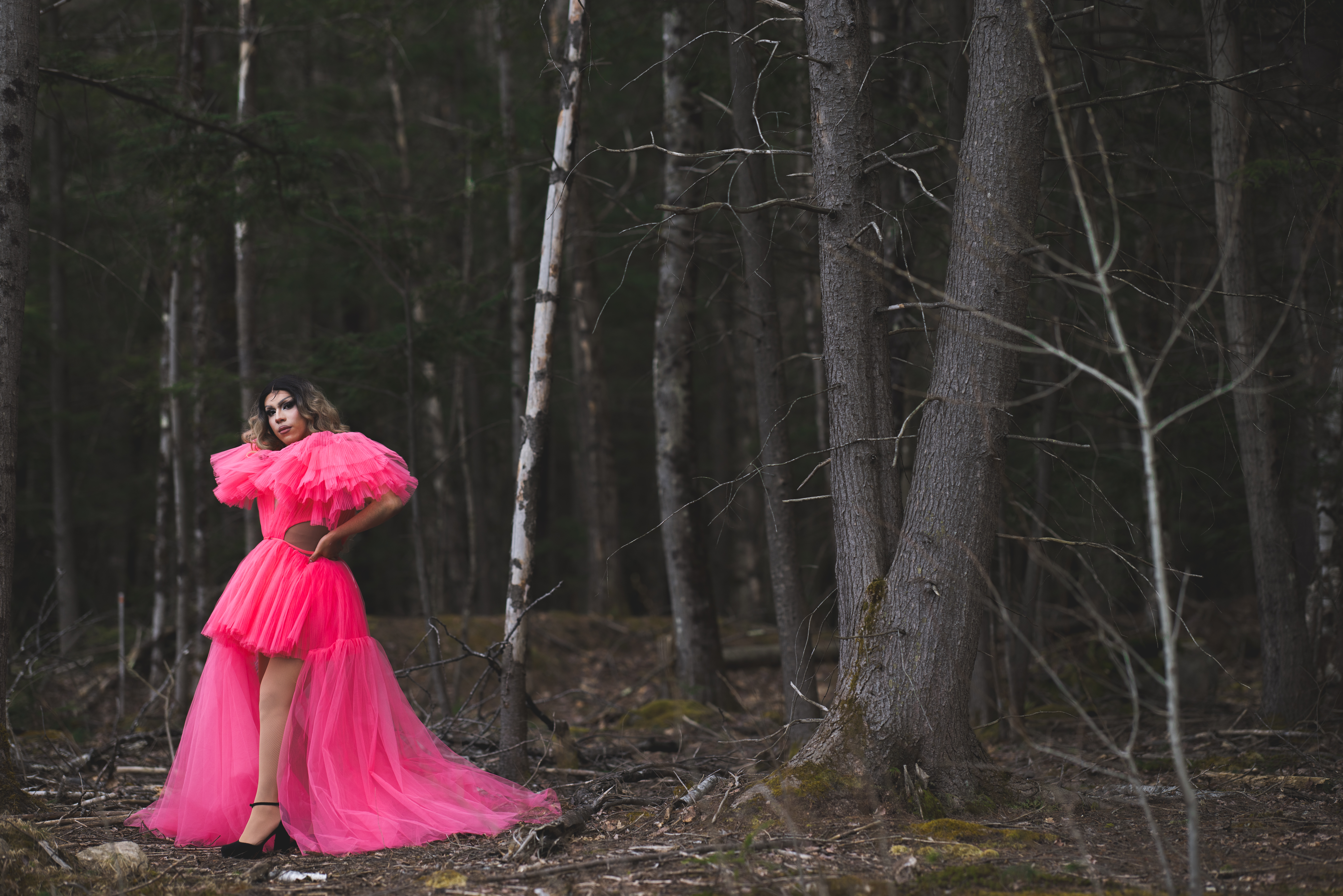 Jaime Aranzabal, dressed in a bright pink dress, stands in the middle of the woods.