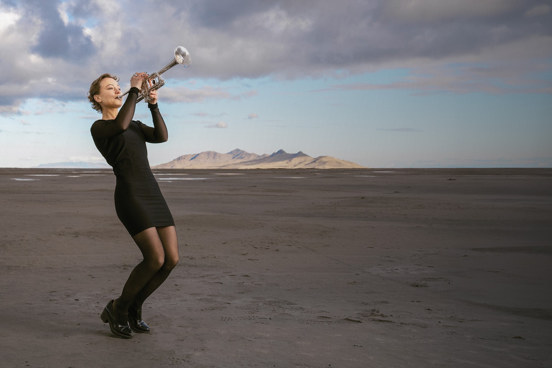 A University of Utah music student in heels and concert dress plays her trumpet on the Great Salt Lake mudflats.