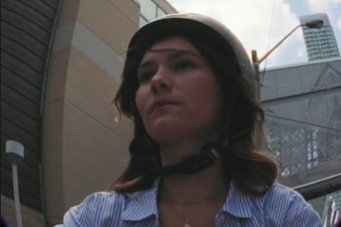 Through a fisheye lens, a close-up of a TMU student riding a bike through Toronto. She wears a black helmet.