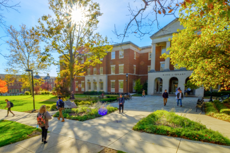 A shot of campus shows the sun rising through tree branches and students walking to and from the library.
