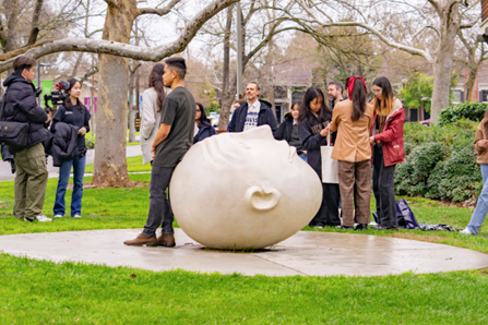 UC Davis students gather around one of the Egghead statues. One student leans against the head to pose for a picture.