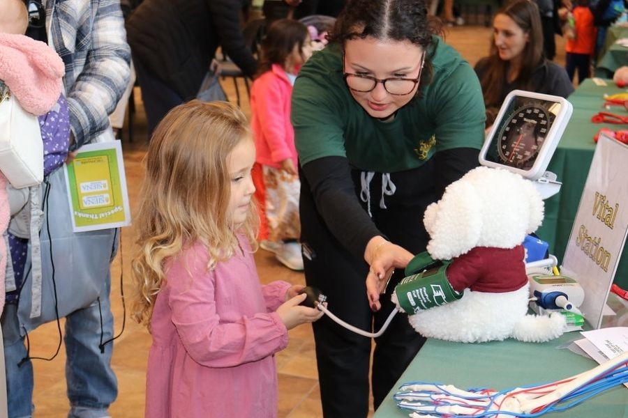 Young girl and college student check the blood pressure of a stuffed animal at Siena University