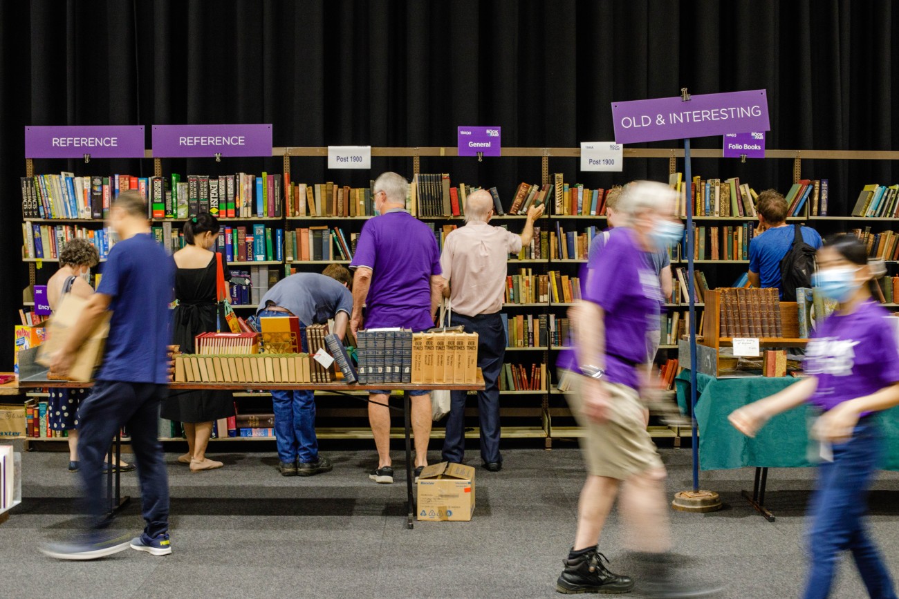 UQ community members browse at the UQ Alumni Book Fair, as UQ volunteers in purple shirts work the fair.