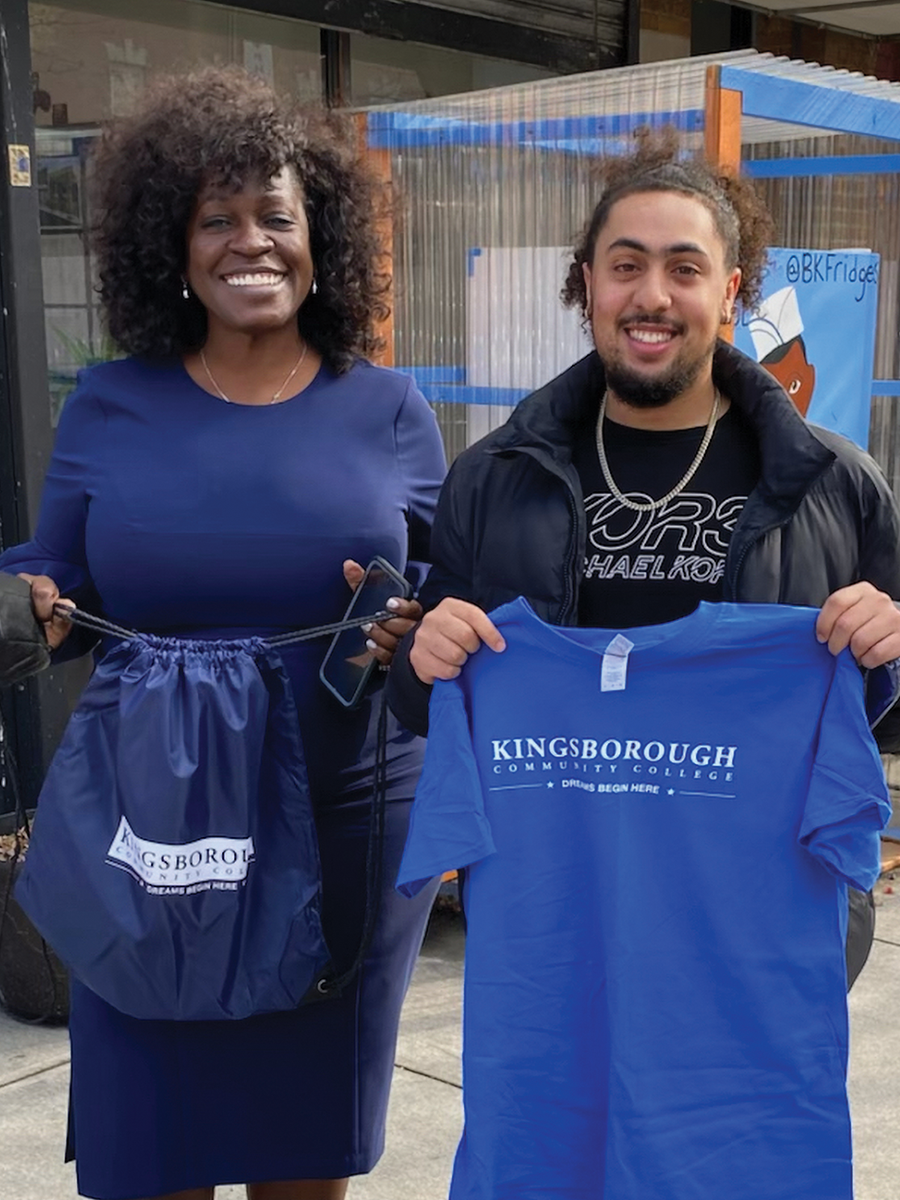 Photo of Kingsborough Community College President Claudia Schrader giving a t-shirt to incoming student