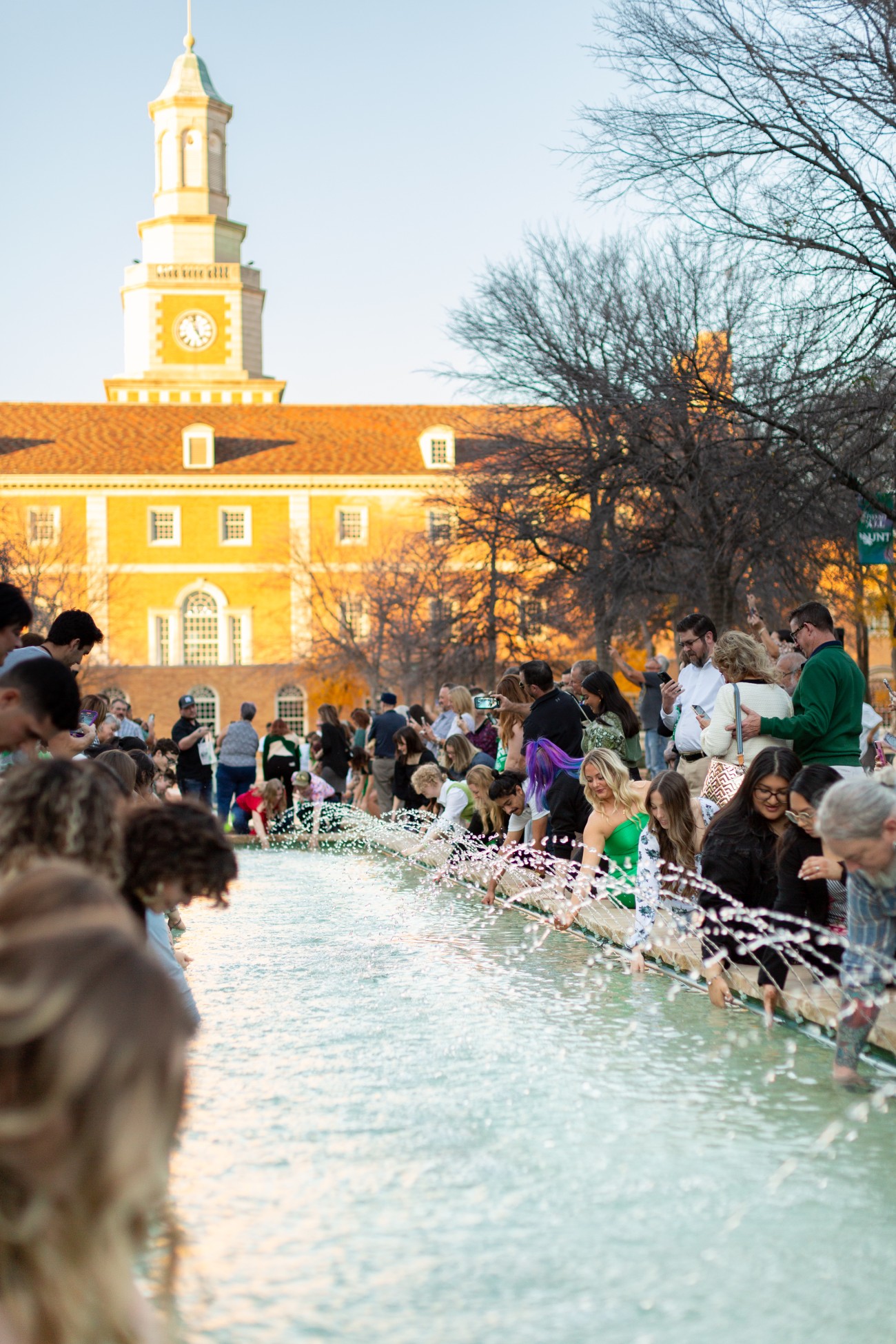 A medium shot shows UNT graduates participating in the Eagle Ring Dive--dipping their new class rings into a campus fountain.