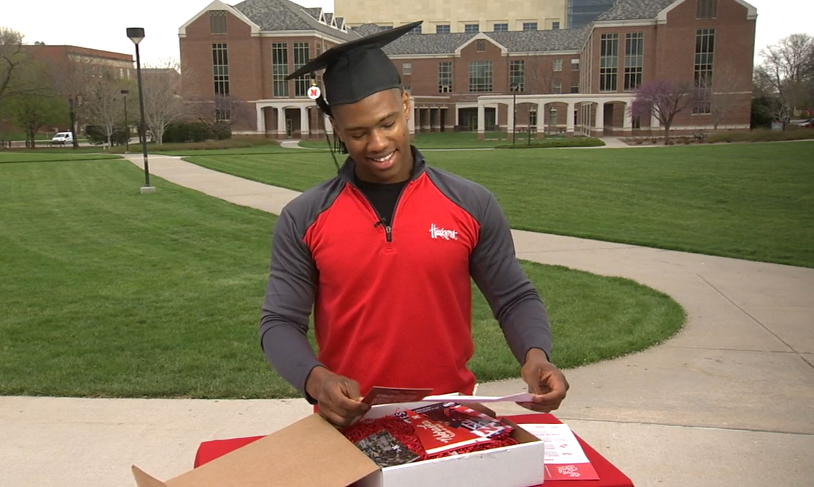 student in a graduation cap unboxing a celebration box on University of Nebraska Lincoln's campus