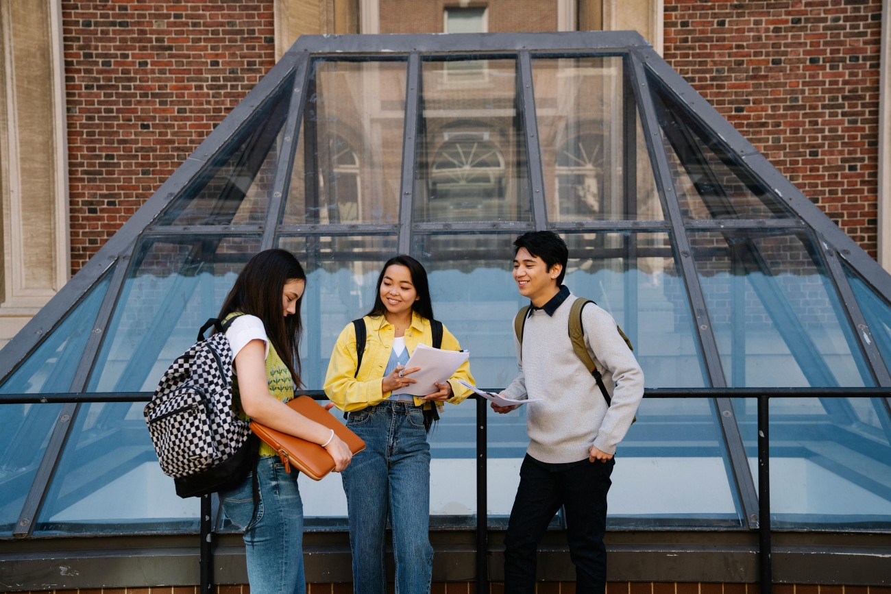 Three students speaking outside of a glass window