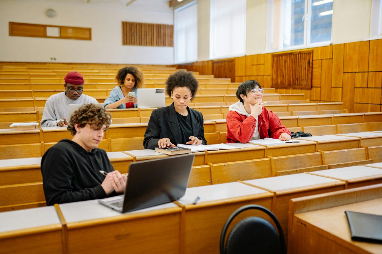 Several students inside a lecture hall talking and looking at a computer