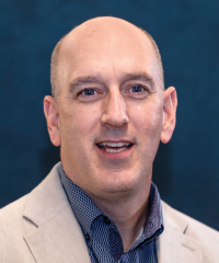 Headshot of Grant Kollet. He wears a blue button down and tan sportscoat.