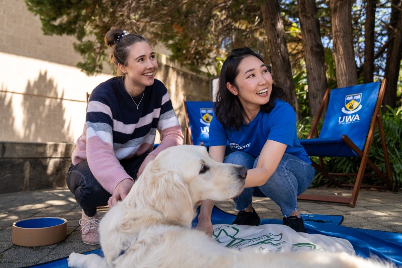 Two UWA students kneel next to a dog.
